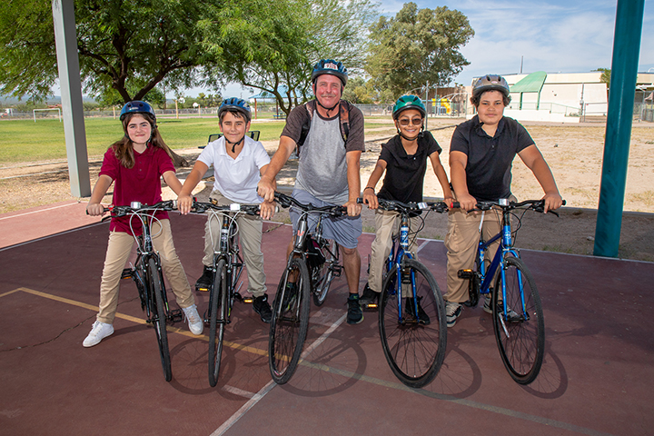 Four students and their teacher pose on their bikes outside